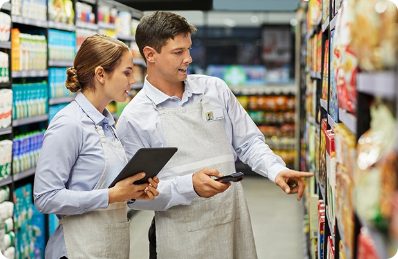 Two field marketing professionals analyzing product placement in a grocery store, focusing on promotional compliance and shelf visibility.