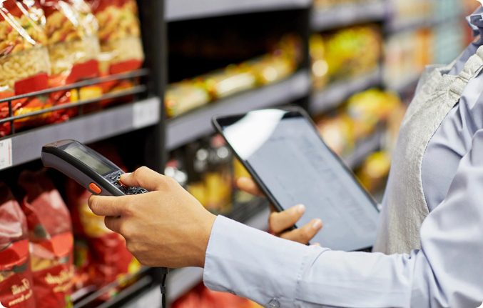 A field marketing professional using a handheld device and tablet in a retail store to ensure product availability and compliance in FMCG.