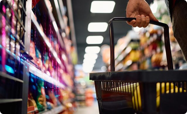 Customer holding a shopping basket in a brightly lit FMCG retail aisle filled with products, showcasing a vibrant shopping environment.