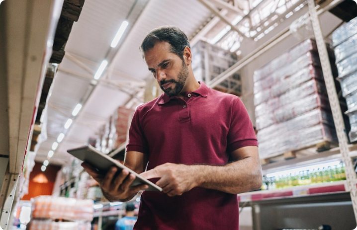 A field marketing professional in a red polo shirt is engaged with a tablet in a retail space, focusing on store execution and compliance.