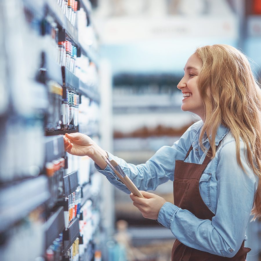 A smiling female field marketing specialist checking product availability on a retail shelf, showcasing effective brand representation in an FMCG environment.