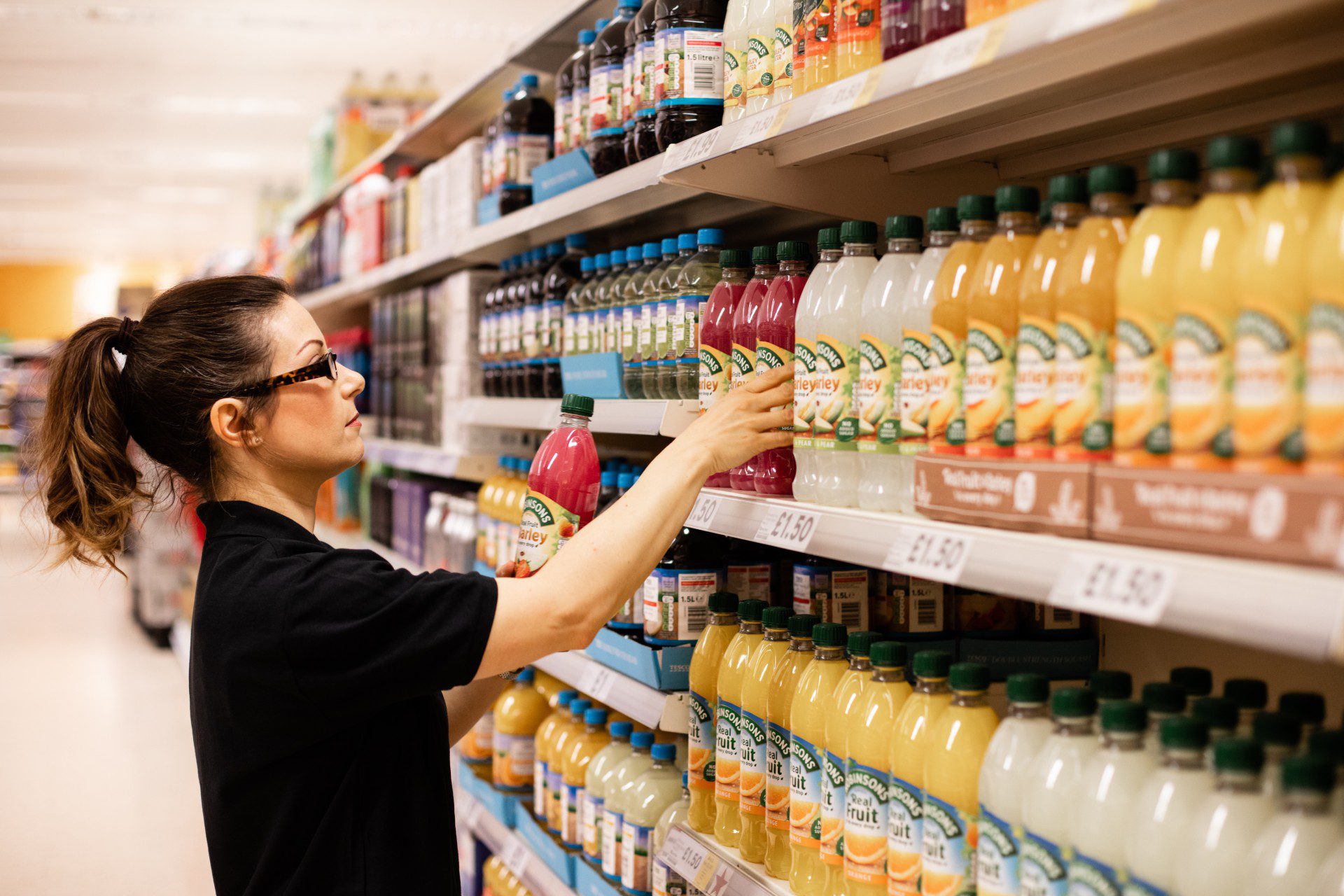 A field marketing professional organizing beverage bottles on a supermarket shelf, illustrating in-store compliance and product availability in FMCG retail execution.